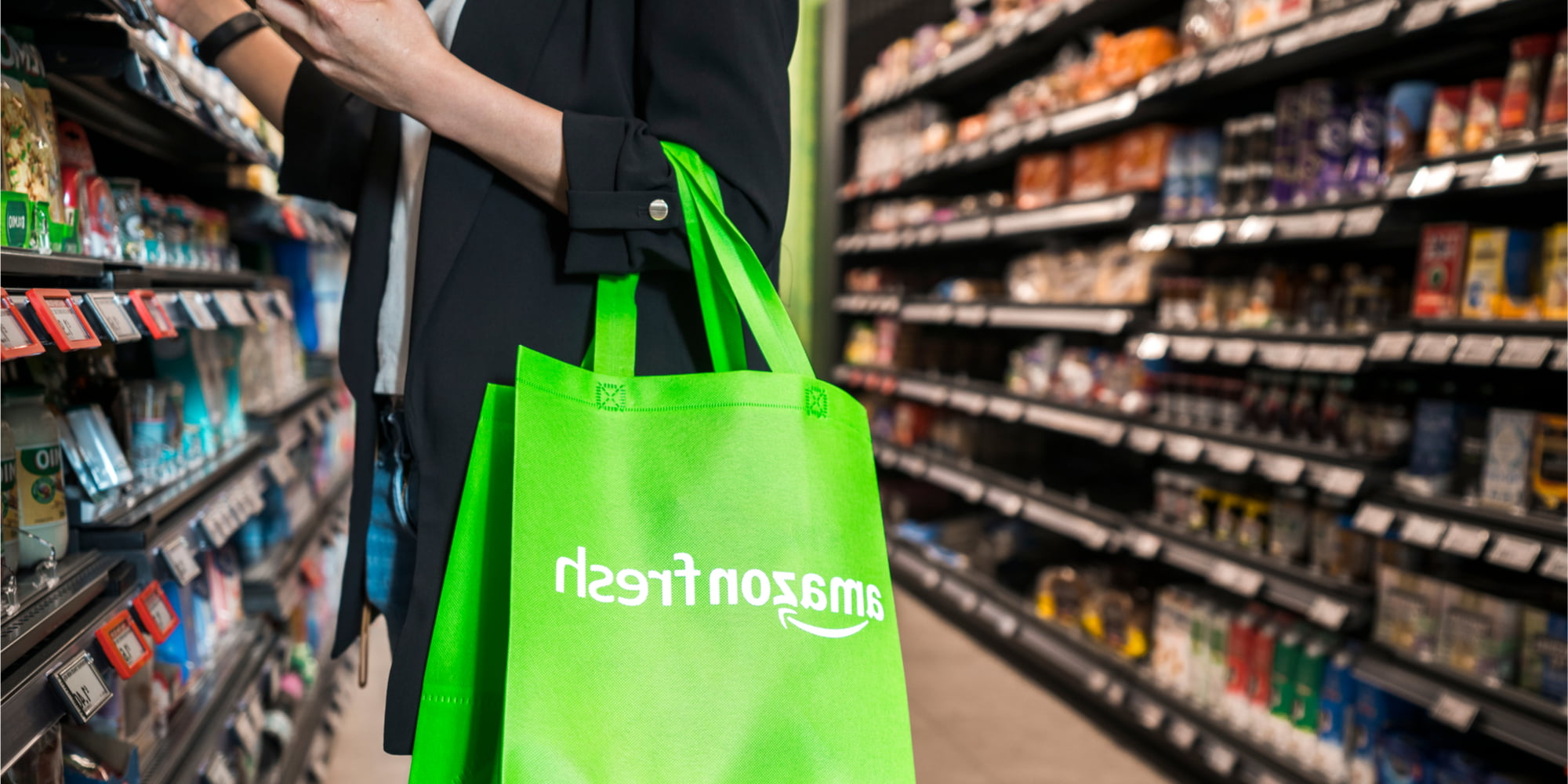 一个人在杂货店的过道里拿着一个柠檬绿色的亚马逊新鲜可重复使用的袋子. 