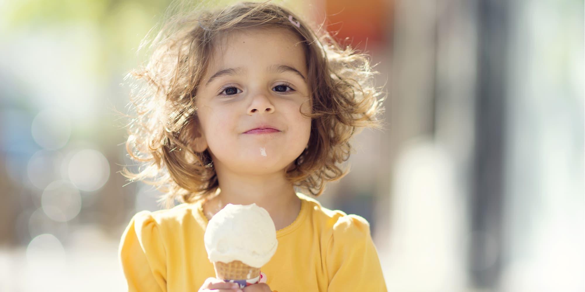 穿黄色衬衫的小女孩吃着香草冰淇淋